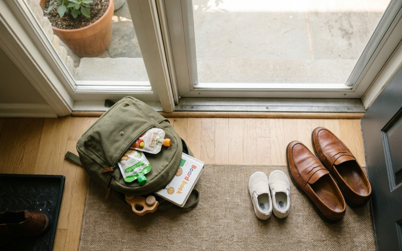 Packed kids' backpack with snacks and toys beside adult and children's shoes at the front door before a home showing